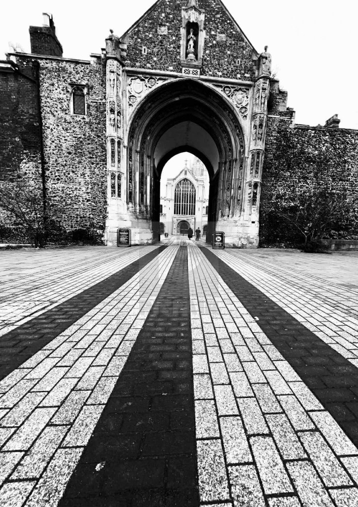 A high contrast black and white photograph of the historic stone gateway to Norwich Cathedral