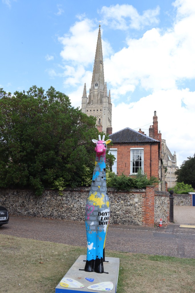 Photograph of a brightly painted giraffe sculpture on a concrete plinth.